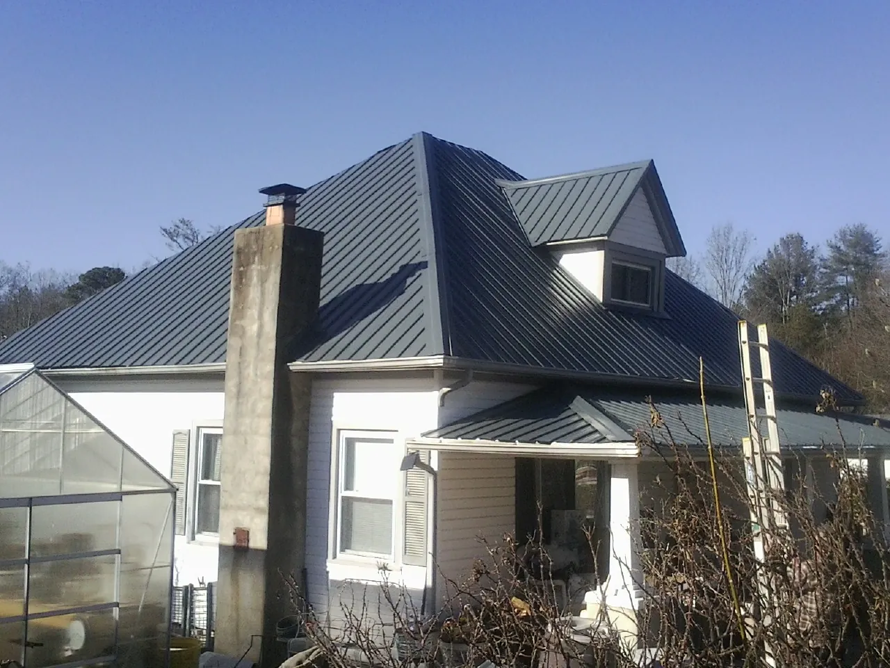 Dark blue standing seam metal roof on a white farmhouse with dormer — Slate & Tile Roof Repair by Roofing Brothers in Massapequa Park