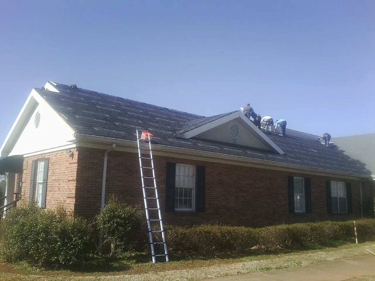 Crew tearing shingles off a brick ranch roof with a ladder set — Metal Roof Repair work by our crew in Massapequa Park
