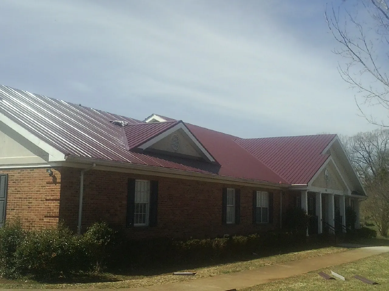 Red metal roof with gabled entries on a long brick building, from a Hail Damage Roof Repair job in Massapequa Park