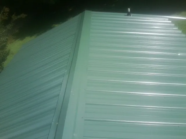 New green metal panels meeting at the ridge of a roof — Flat Roof Repair work by our crew in Massapequa Park