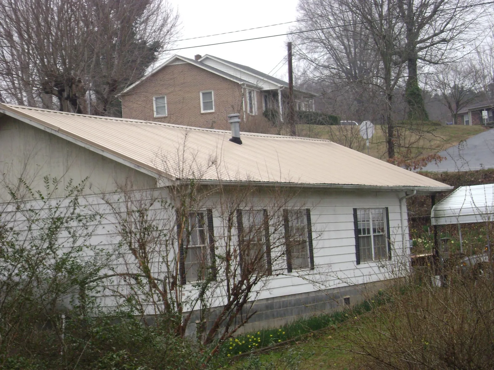 Tan metal roof on a white sided house set into a hillside — Commercial Roofing by Roofing Brothers in Massapequa Park